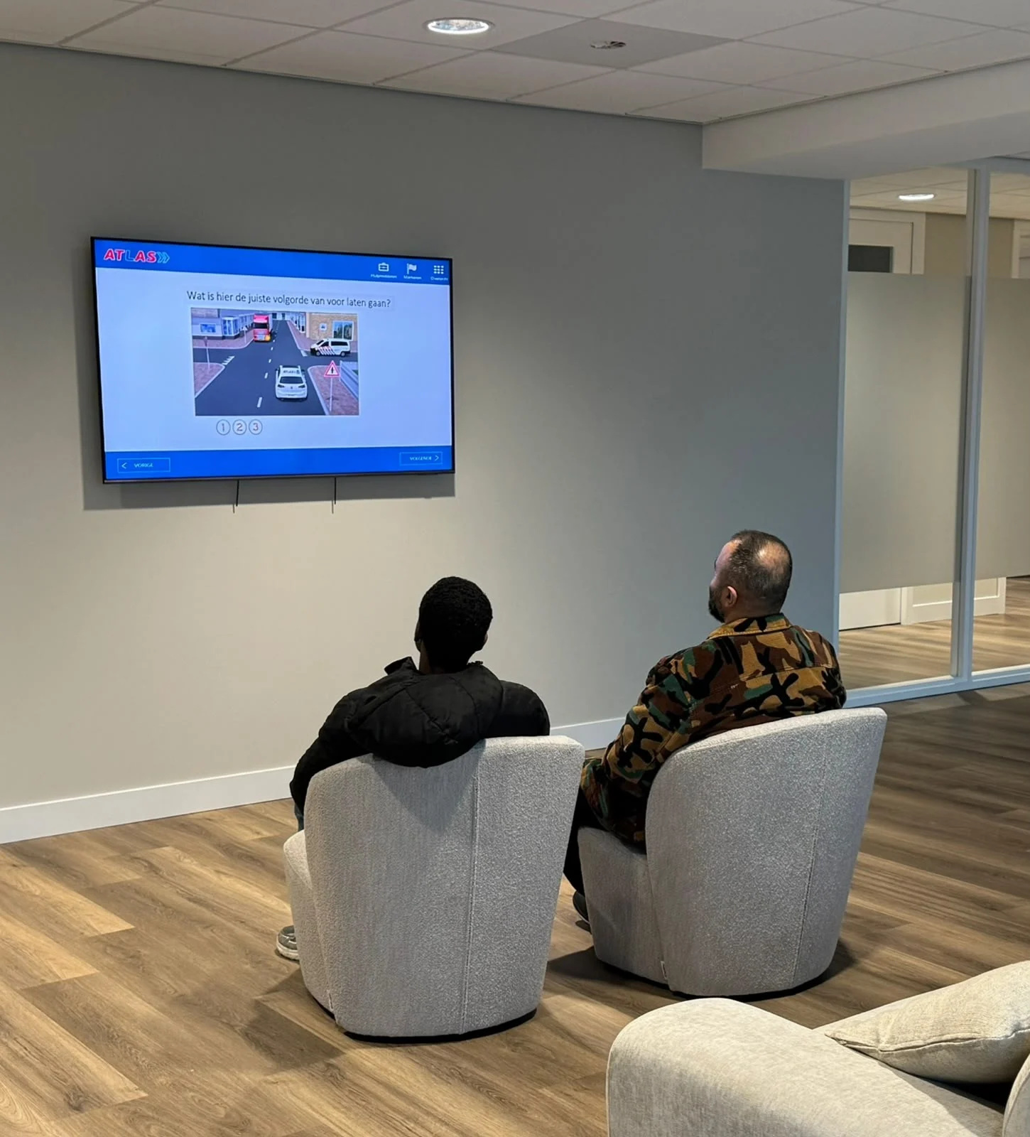 Een begeleider helpt een jongere bij de voorbereiding op zijn auto-theorie examen, met een theorievraag op het scherm
